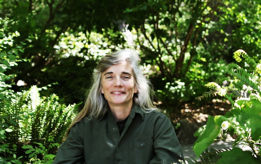 Appalachian author, Ann Pancake, poses for a photo against a lush, green background,